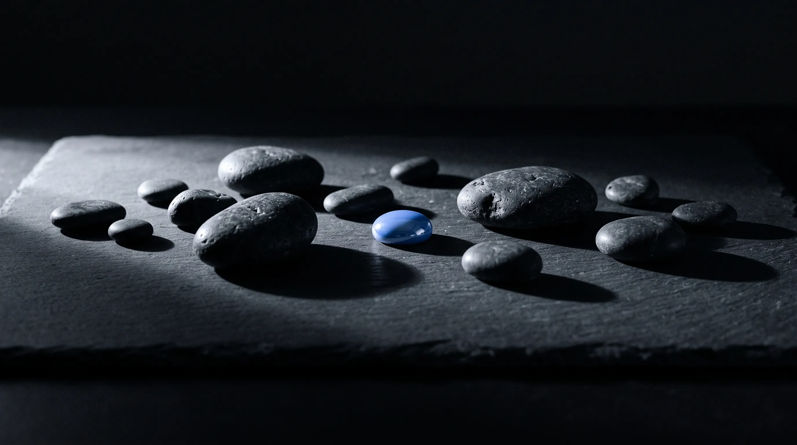 Piedras oscuras repartidas como un archipiélago sobre pizarra; una de ellas, azul y brillante