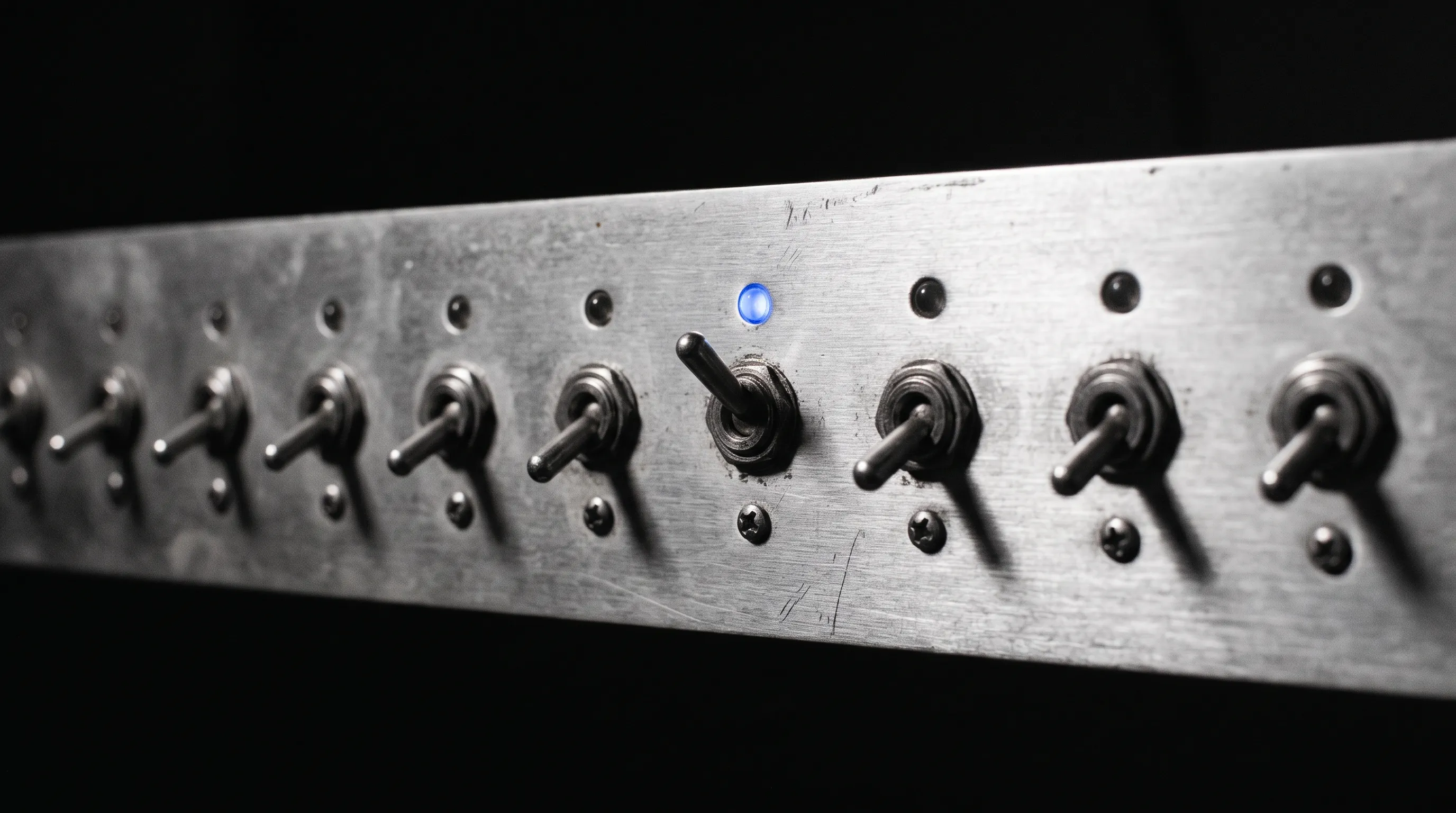 Panel de interruptores metálicos; uno levantado, con su luz azul encendida